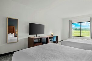 Habitación de hotel con dos camas, televisor, escritorio con silla y un amplio ventanal con vistas a un paisaje verde.