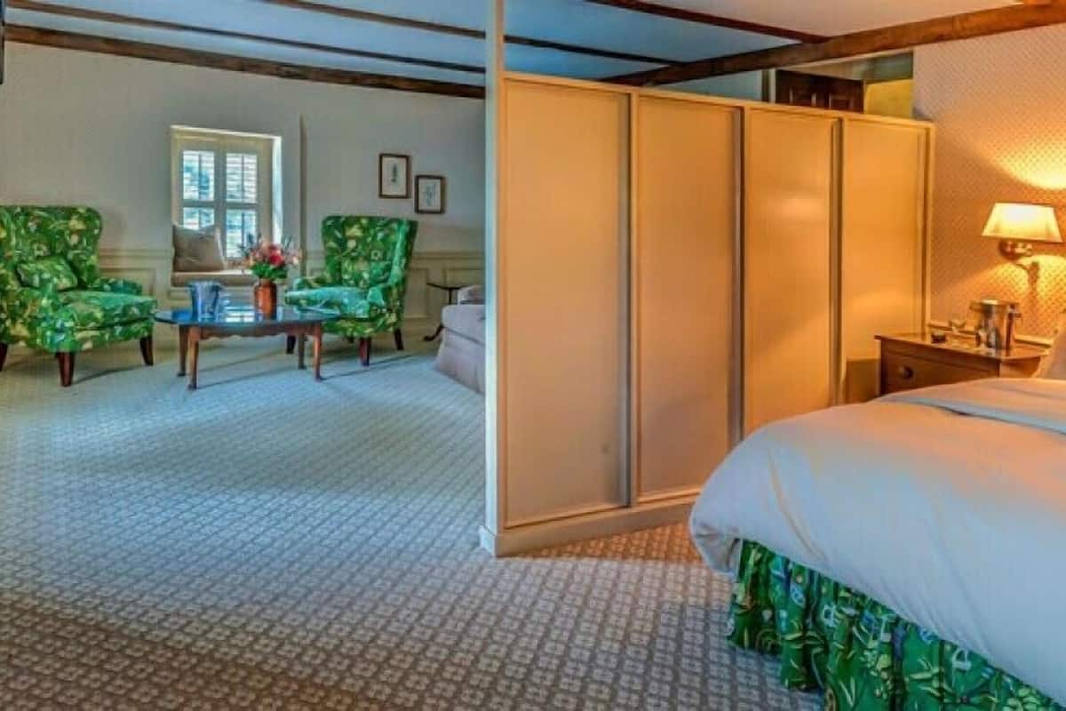 A hotel room with a bed, a desk, two chairs, a wardrobe, and a window.