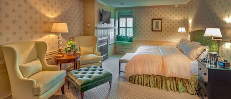 Habitación de hotel con una cama grande, una zona de estar con sofá y sillón, una mesita con lámpara, y vistas al exterior a través de una ventana.