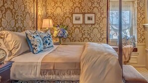 A four-poster bed with a canopy, a nightstand with a lamp, and two framed pictures on the wall. - Golden Plough Inn At Peddlers Village (New Hope)