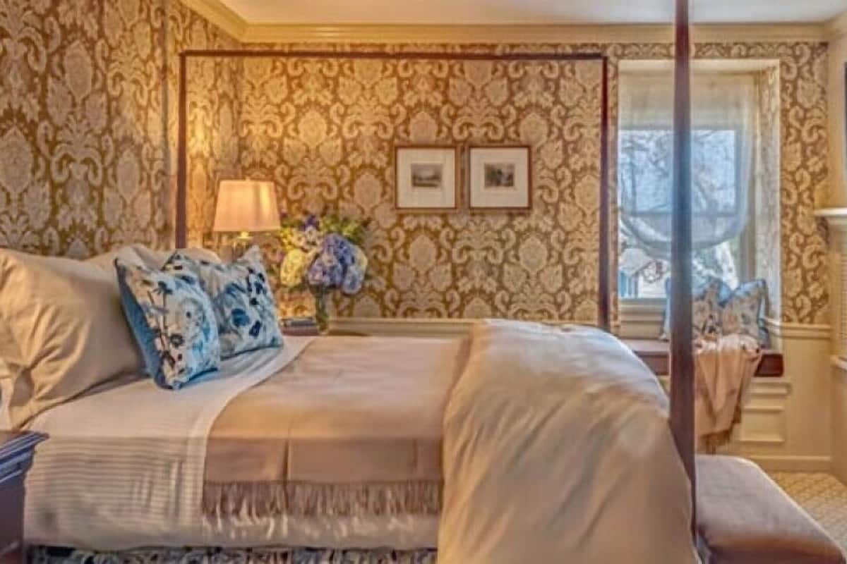 A four-poster bed with a canopy, a nightstand with a lamp, and two framed pictures on the wall.