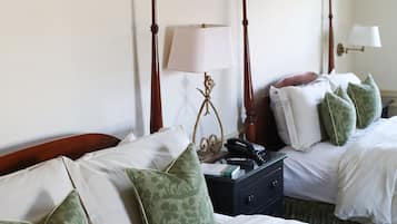 Habitación de hotel con dos camas, cada una con ropa blanca y almohadas estampadas en verde. Entre las camas, hay una mesita de noche con una lámpara y un teléfono.