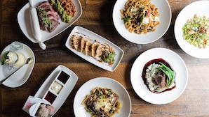A variety of dishes on a wooden table, including pasta, steak, and a salad. - Golden Plough Inn At Peddlers Village (New Hope)