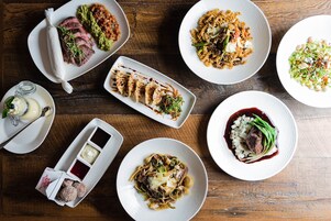 A variety of dishes on a wooden table, including pasta, steak, and a salad.