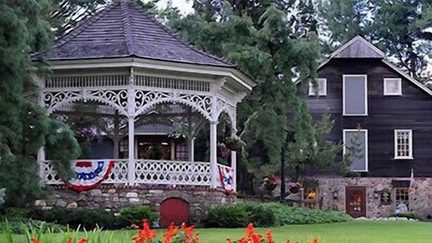 A gazebo with a decorative railing and a house with a stone foundation and a red door. - Golden Plough Inn At Peddlers Village (New Hope)