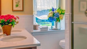A bathroom with two sinks, a window with a view, and a vase with flowers on the windowsill. - Golden Plough Inn At Peddlers Village (New Hope)