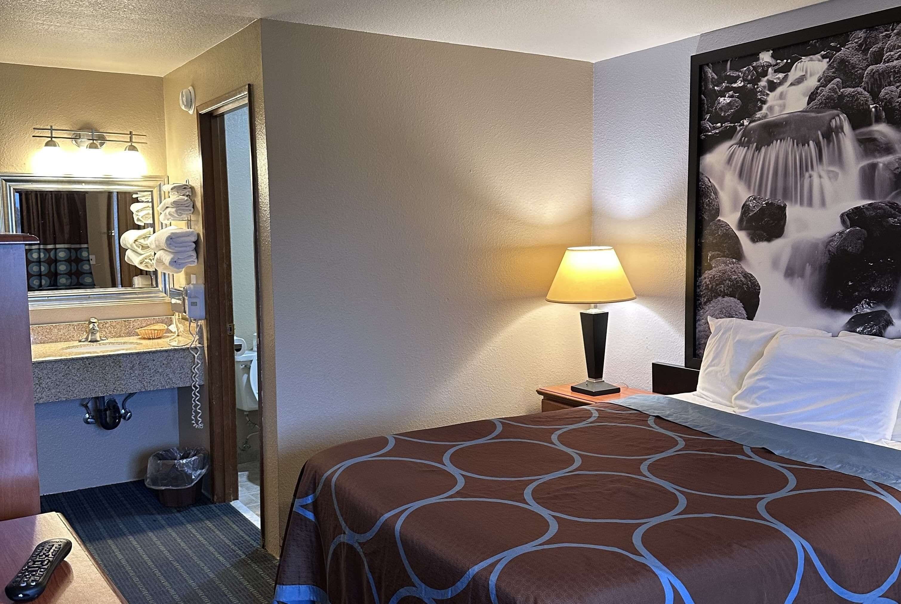 Ein Hotelzimmer mit einem Bett, einem Badezimmer inklusive Waschbecken und Spiegel, einer Lampe sowie einem an der Wand befestigten Fernseher.