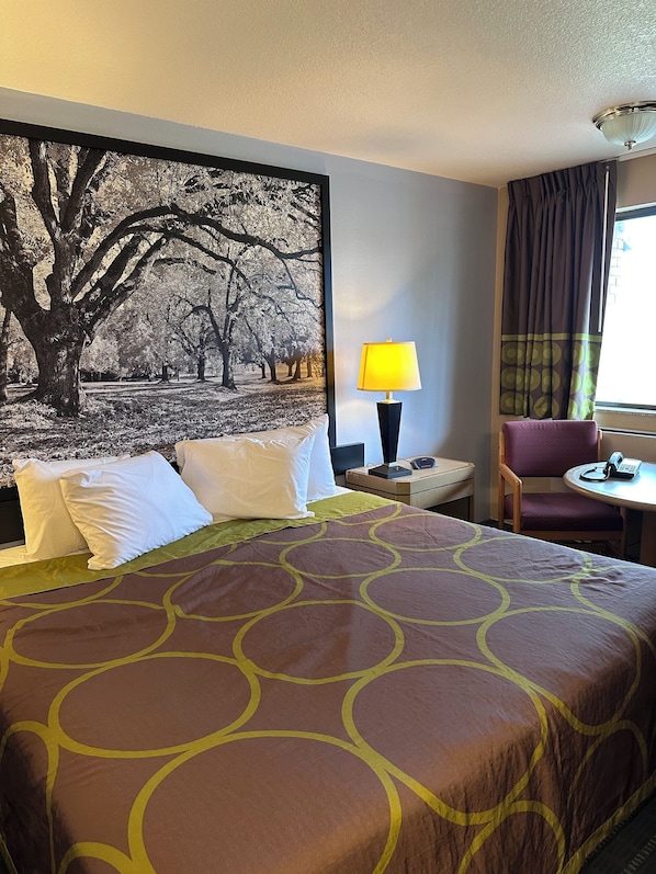 A hotel room with a large bed, a nightstand with a lamp, a chair, and a table.
