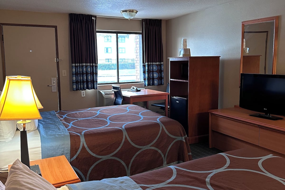 A hotel room with two beds, a desk, a TV, and a window with curtains.
