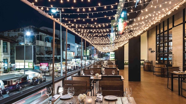 Un espace extérieur aménagé pour les repas, avec des guirlandes lumineuses, des tables en bois et une vue sur la rue.