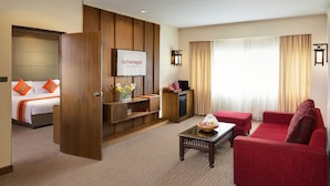 A hotel room with a bed, a red sofa, a coffee table, a TV, and a desk with a lamp.