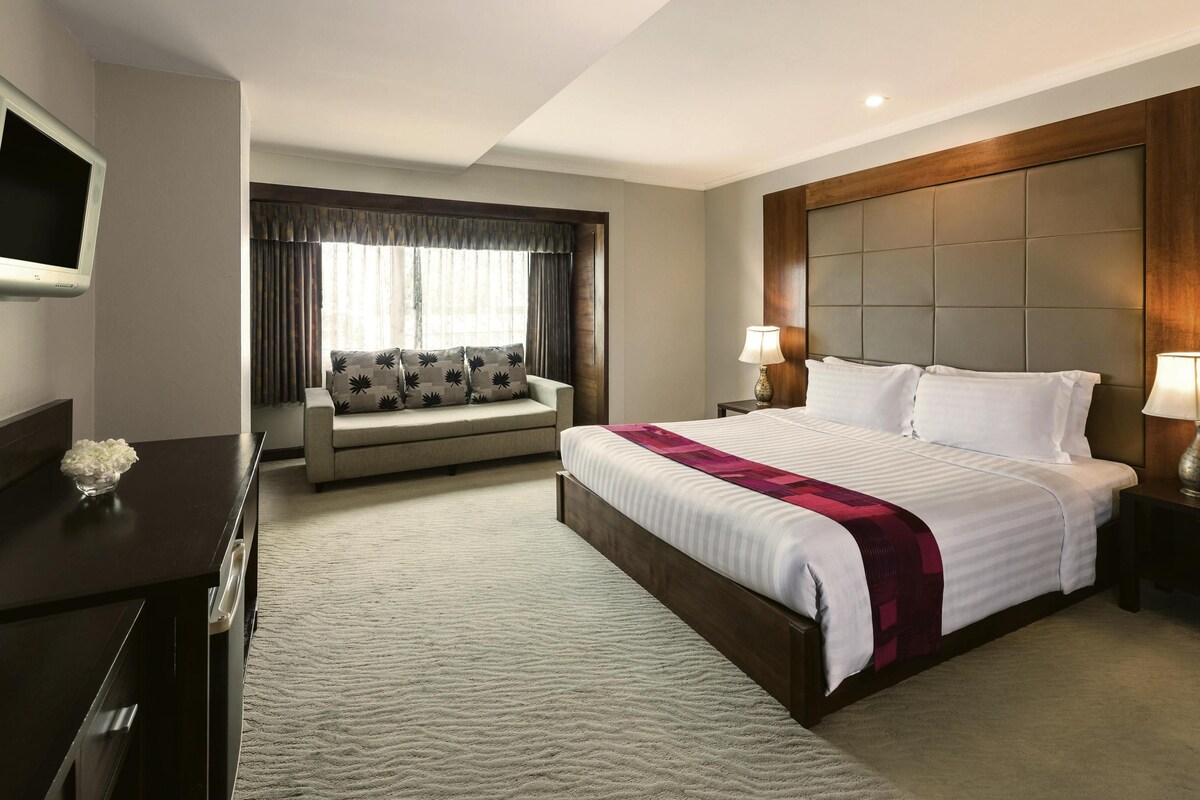 A hotel room with a bed, a sofa, a TV, and a window with curtains.