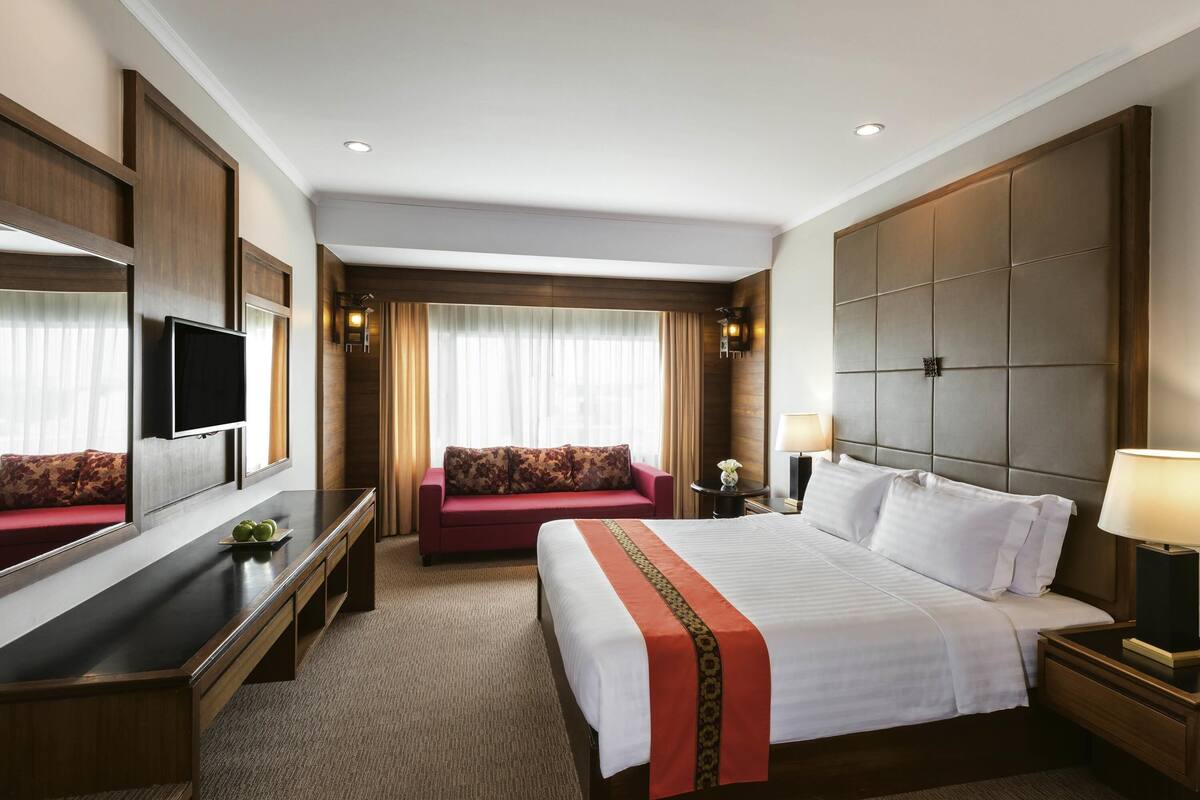 A hotel room with a bed, a sofa, a TV, a desk, and a mirror.