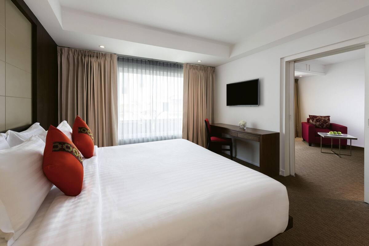 A hotel room with a large bed, a desk, a TV, and a separate seating area.