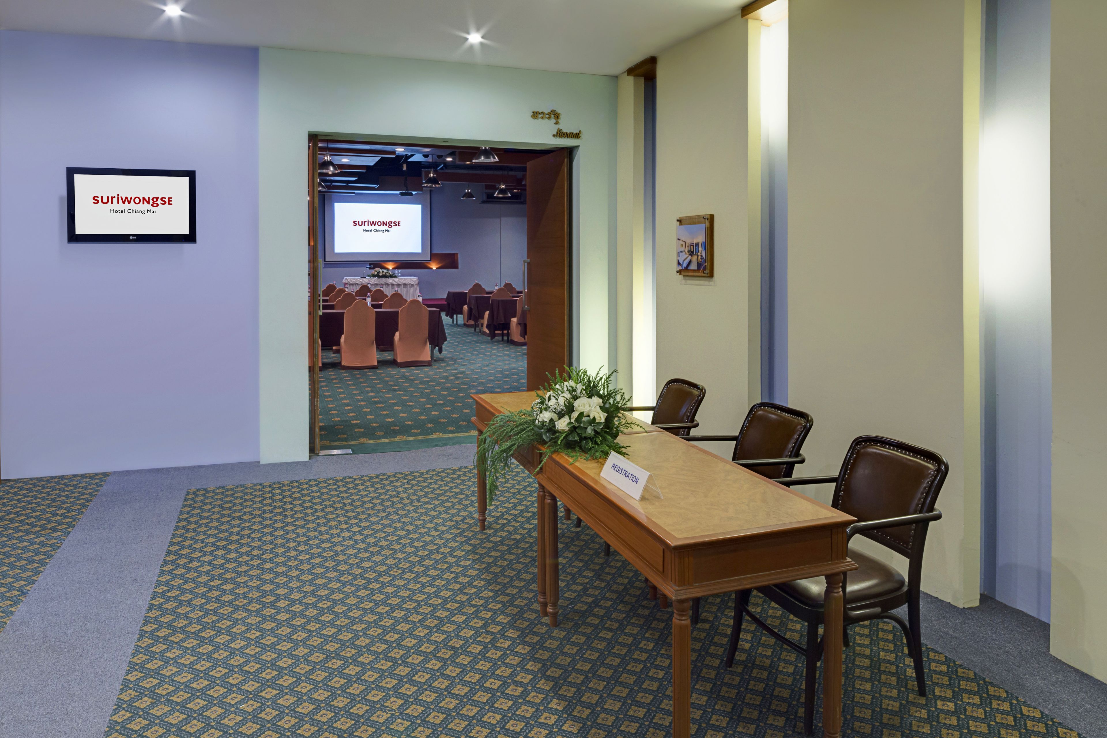 Una sala de conferencias con una mesa de madera, sillas, un arreglo floral y un cartel que indica 'registro'.
