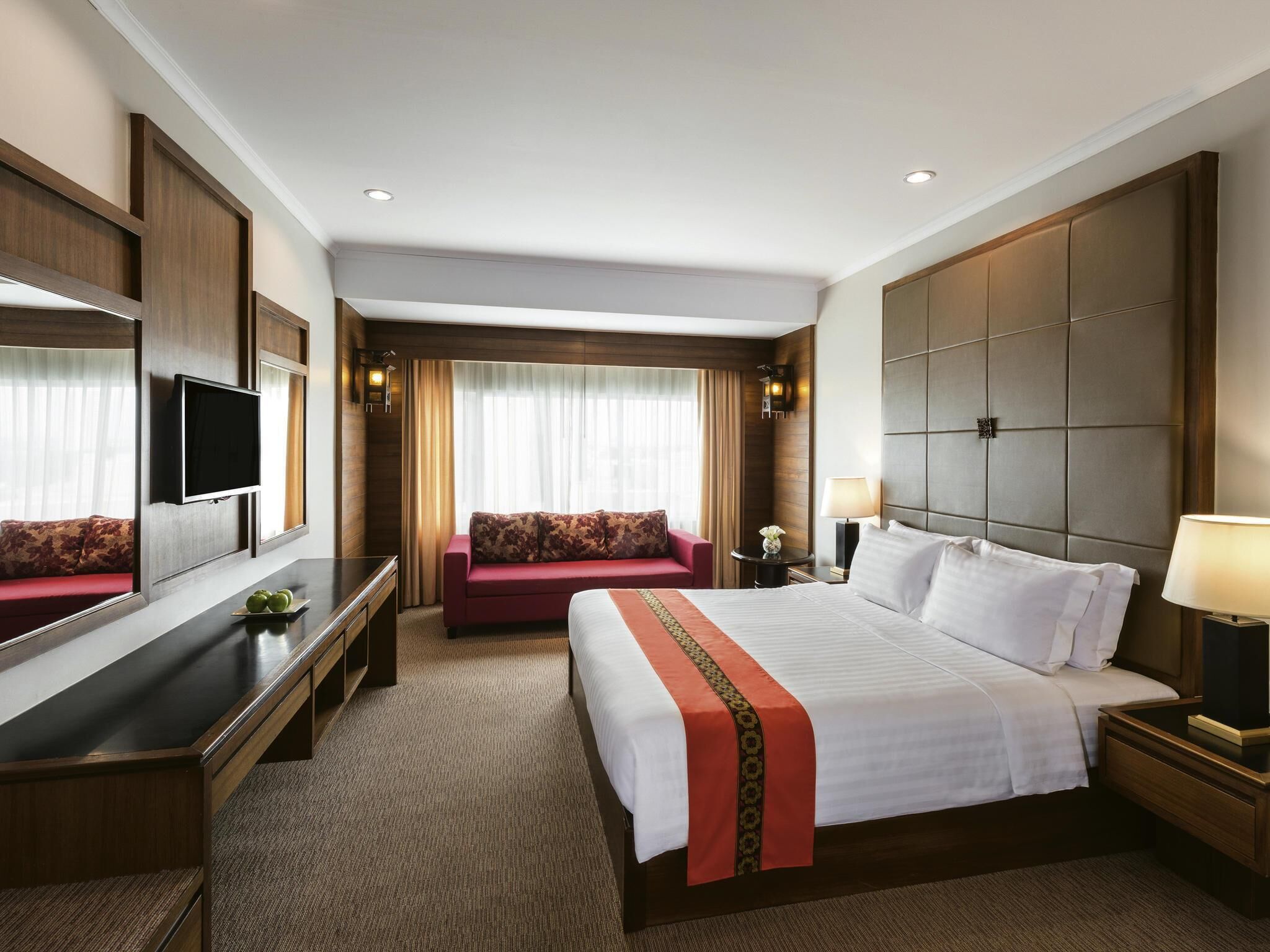 Ein Hotelzimmer mit Bett, Schreibtisch, Sofa, Fernseher und einem großen Spiegel.