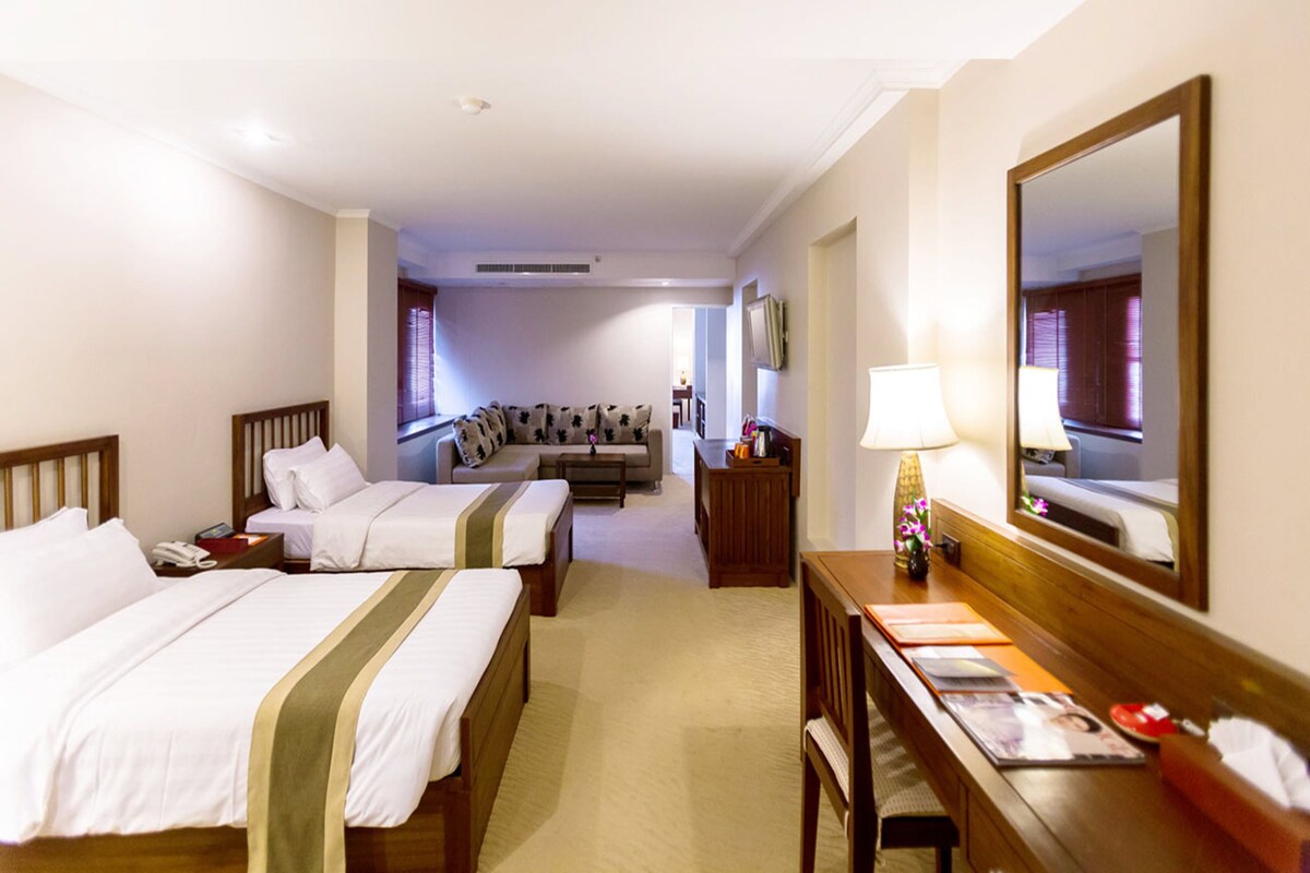 Ein Hotelzimmer mit zwei Betten, einem Schlafsofa, einem Schreibtisch mit Lampe und einem großen Spiegel.