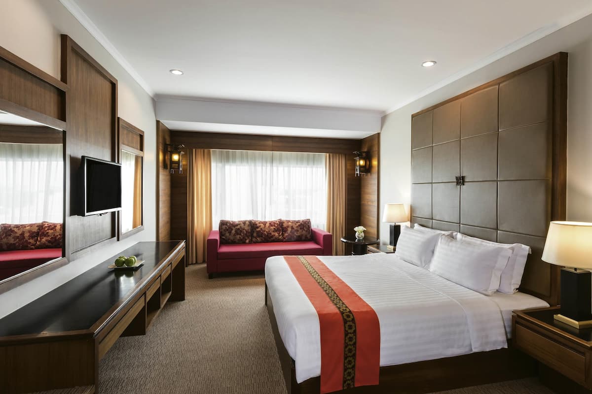 A hotel room with a large bed, a sofa, a TV, and a desk.