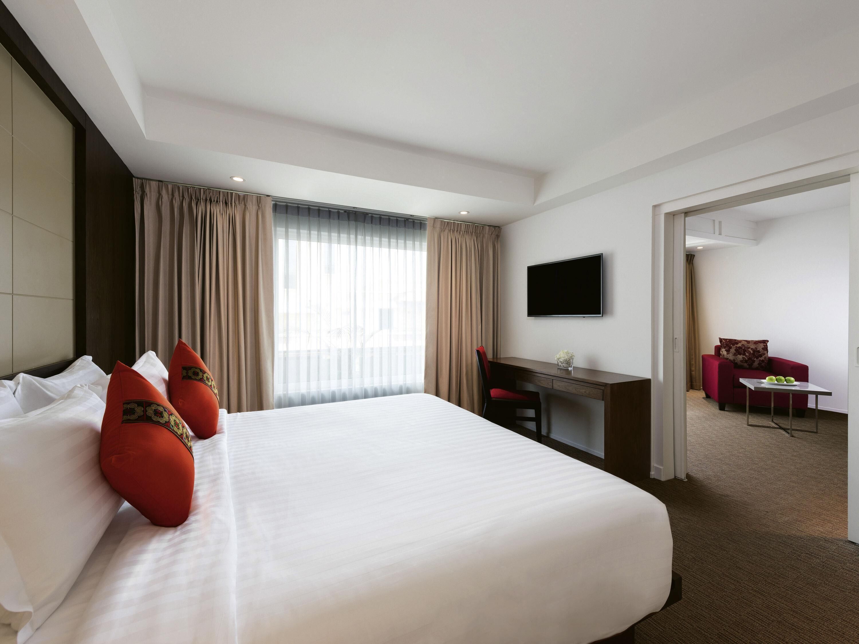 A hotel room with a large bed, a desk, a TV, and a separate seating area.
