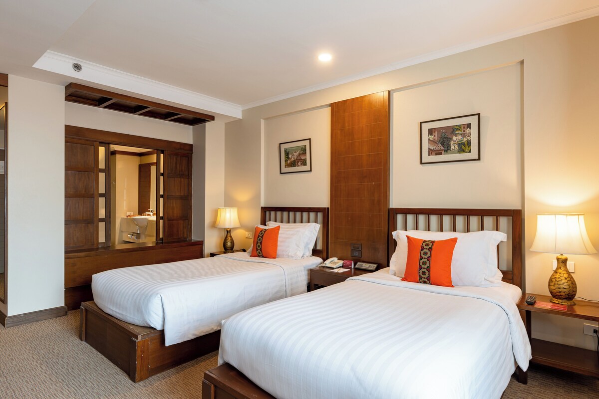 Ein Hotelzimmer mit zwei Betten, Holz-Kopfteilen, einem großen Spiegel und zwei Wandleuchten.