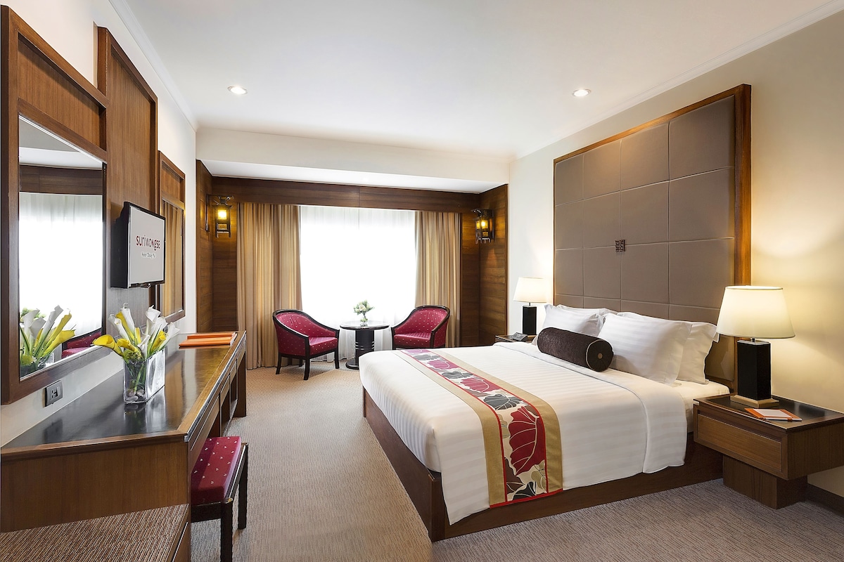Ein Hotelzimmer mit einem großen Bett, einem Schreibtisch mit Stuhl, einem kleinen Tisch für zwei Personen und einem großen Spiegel.