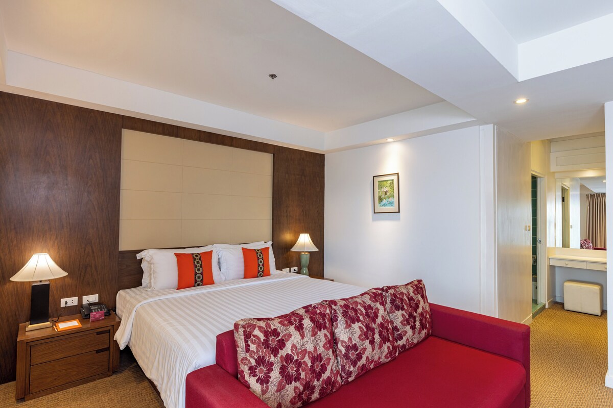 Ein Hotelzimmer mit einem großen Bett, zwei Nachttischlampen, einem roten Sofa und einem hölzernen Kopfteil.