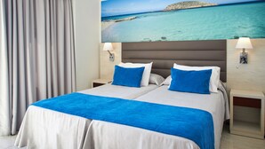 A double bed with a blue and white bedspread, two pillows, a headboard, bedside lamps, and a painting of a beach scene above the bed. - Invisa Hotel Ereso All Inclusive (Santa Eulalia del Rio)