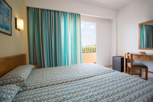 Habitación de hotel con cama, escritorio, silla, basurero y balcón con cortinas.