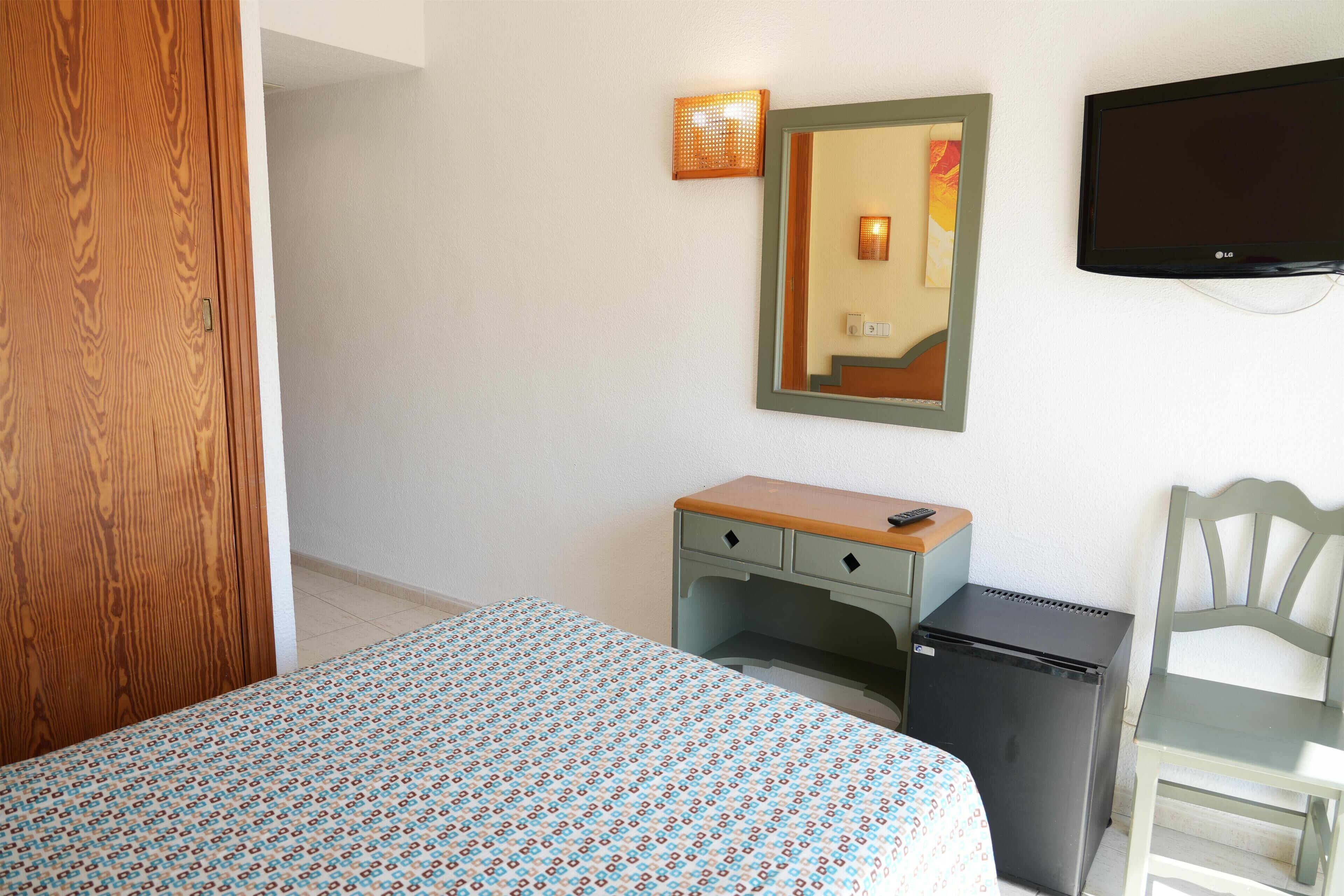Habitación de hotel con cama, escritorio, silla, refrigerador pequeño, televisión y lámpara de pared.