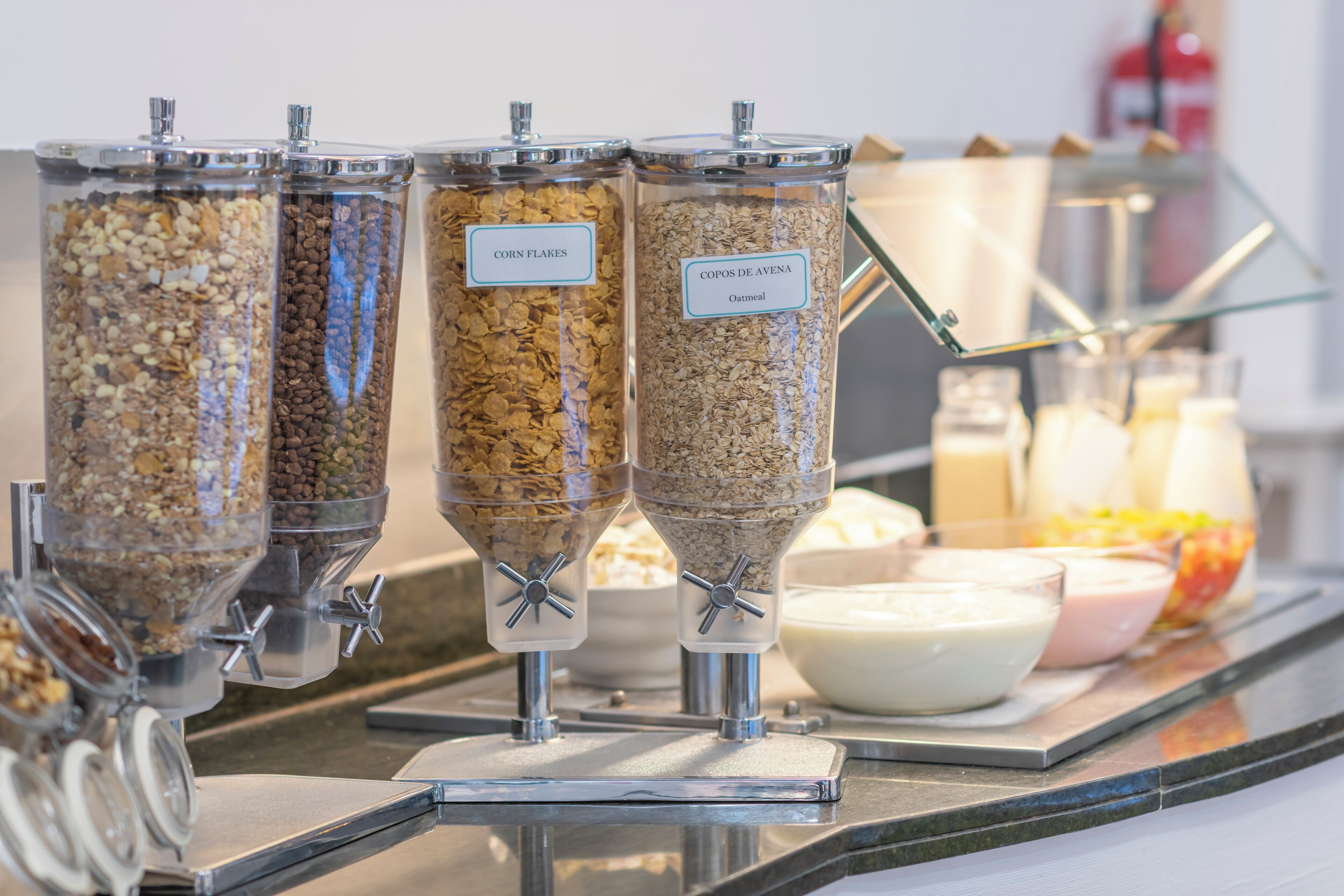 A self-serve breakfast station with labeled containers of cereal and oatmeal.