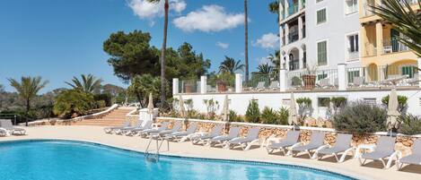 A pool area with lounge chairs and a building with balconies.