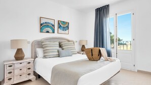 Een slaapkamer met een bed, twee nachtkastjes, een grote raam met gordijnen en twee kunstwerken aan de muur.