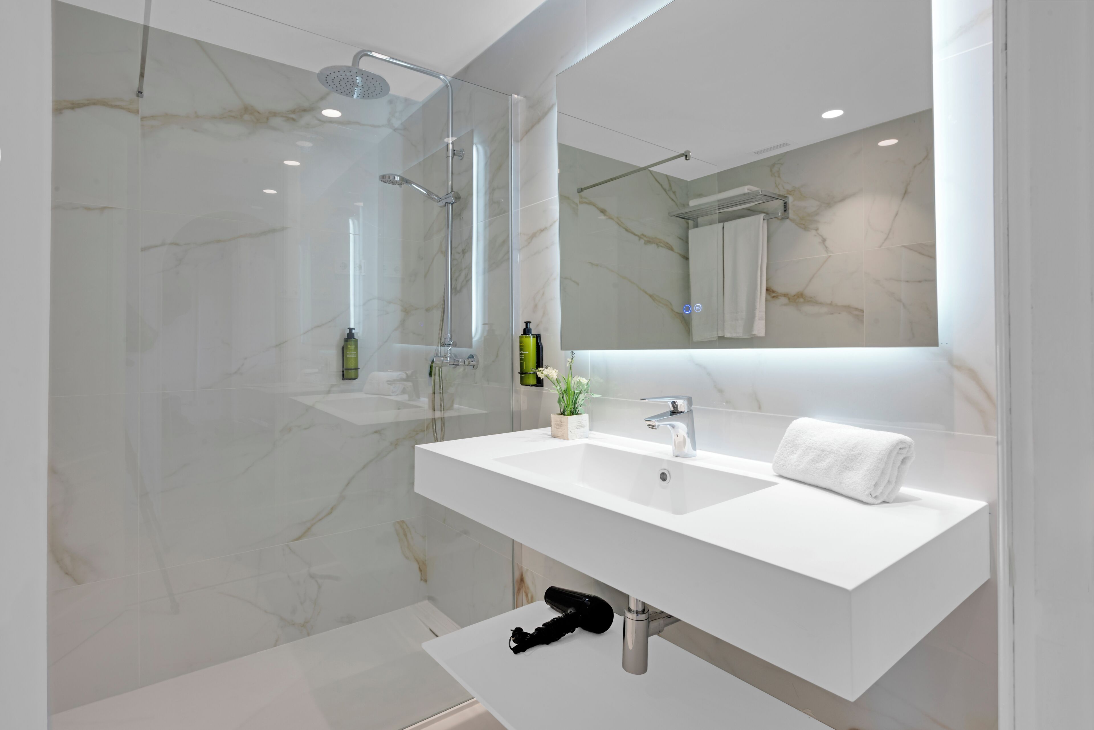 A modern bathroom with a glass-enclosed shower, a white sink with a mirror above it, and a towel on the sink.