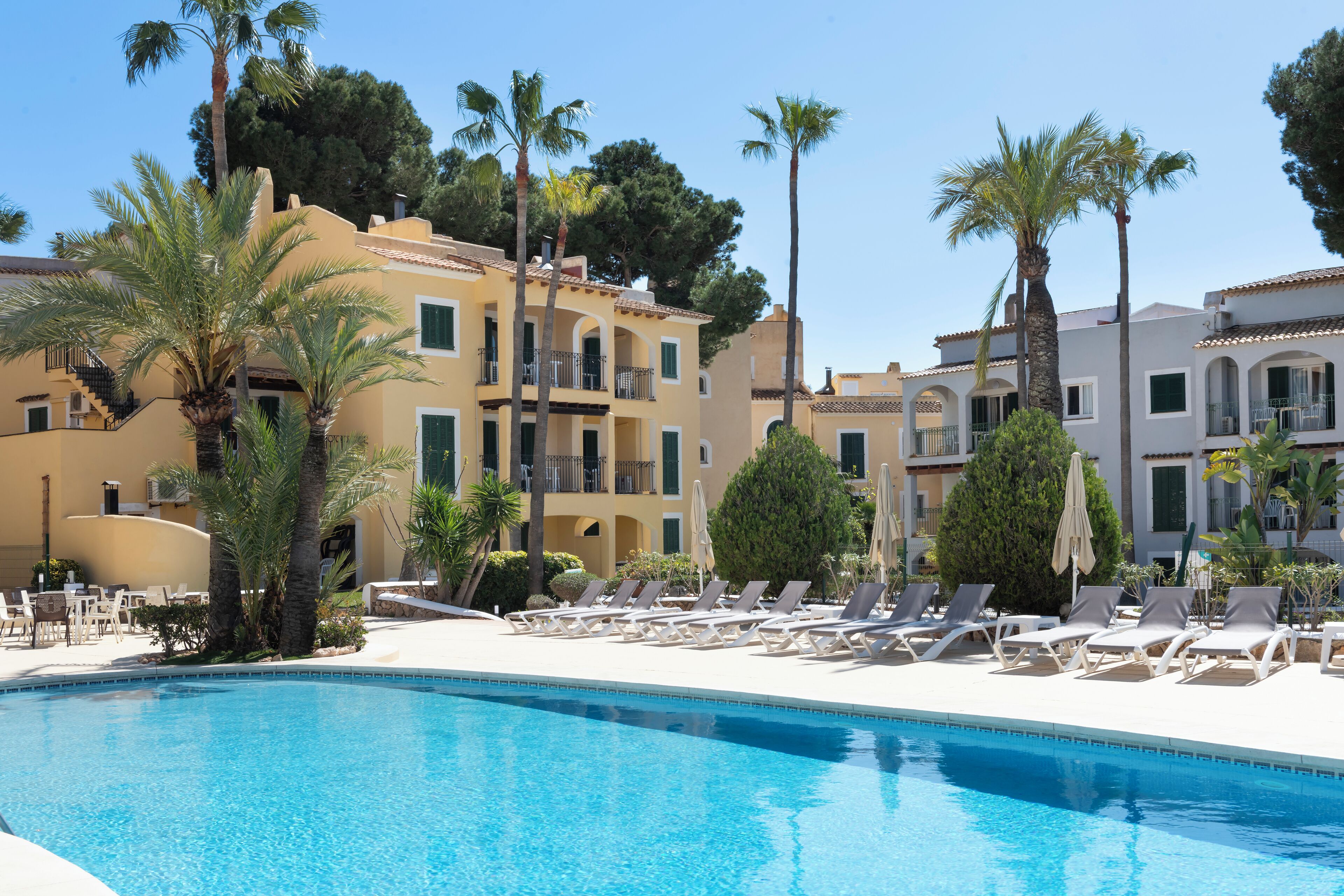 A pool area with lounge chairs and palm trees, surrounded by multi-story buildings with balconies.