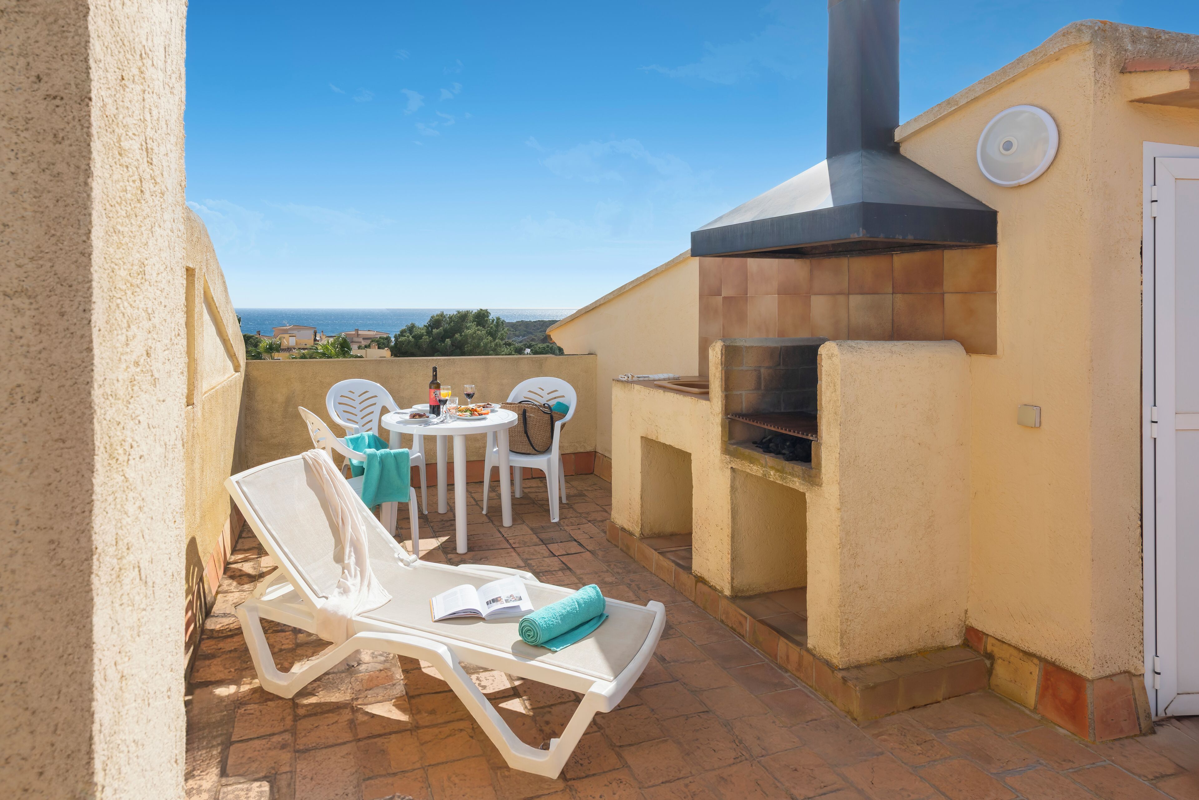 Une terrasse avec un barbecue, des chaises longues et une table avec des chaises.