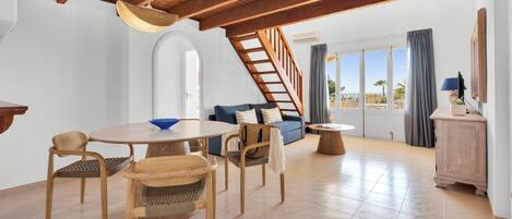 A spacious living area with a wooden ceiling, a round dining table with chairs, a sofa, and a view of the outdoors.