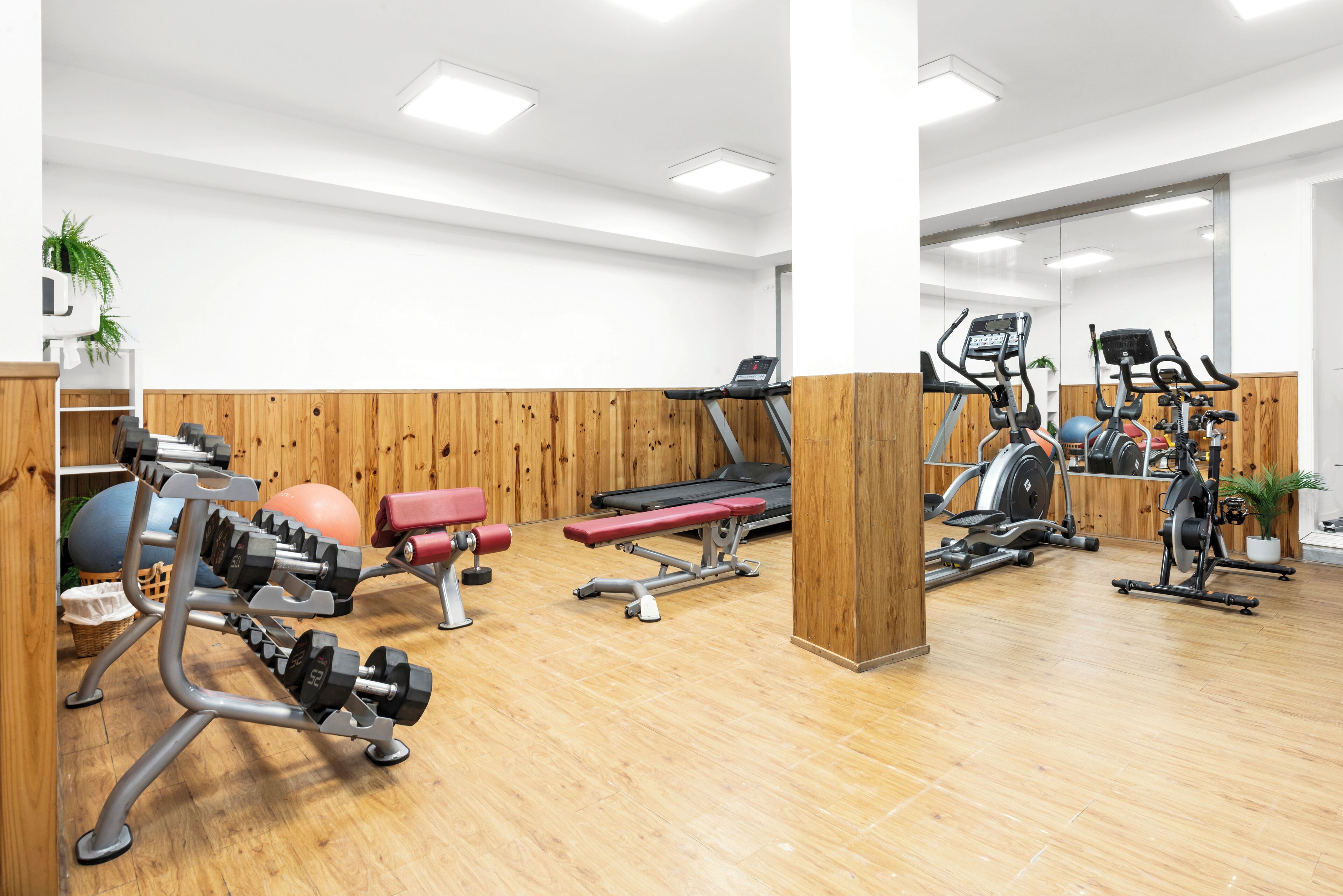 Une salle de sport équipée de matériel d’exercice, dotée d’un plancher en bois et de murs blancs.