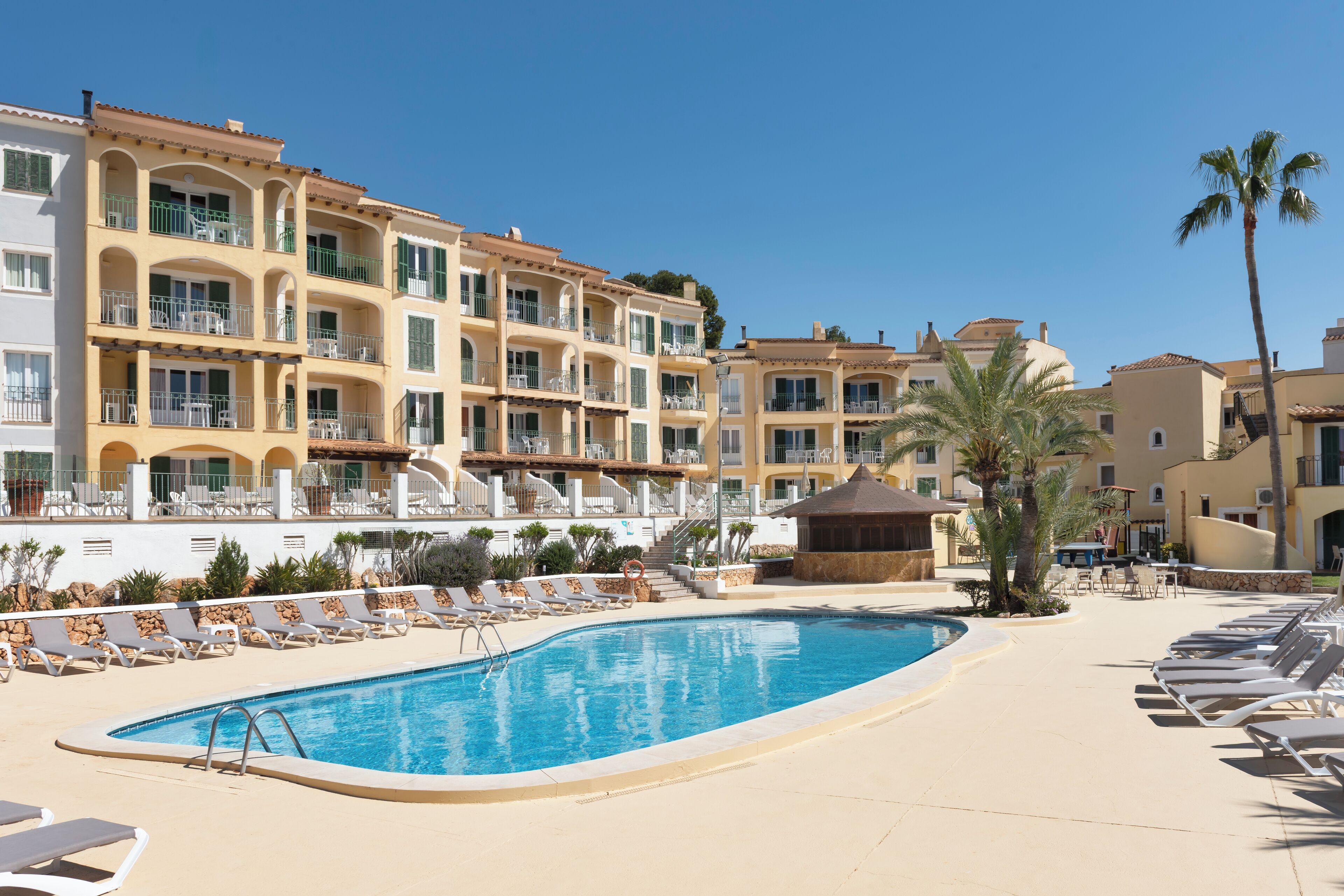 A resort with a swimming pool, sun loungers, and a multi-story building with balconies.