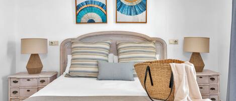 A neatly made bed with striped pillows, a beige blanket, and a woven bag on the side.