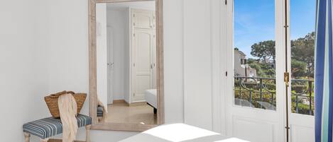 A bedroom with a large mirror, a bed, a bench with a cushion, and a view of the outside through a door.