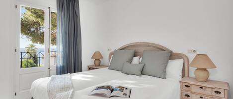 A bedroom with a bed, a nightstand, a lamp, and a view of the outdoors.