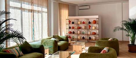A modern living room with green sofas, a glass coffee table, and a pottery shelf.