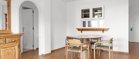 Un coin repas comprenant une table ronde, quatre chaises en bois, un buffet en bois et un mur blanc avec une fenêtre située au-dessus du buffet.