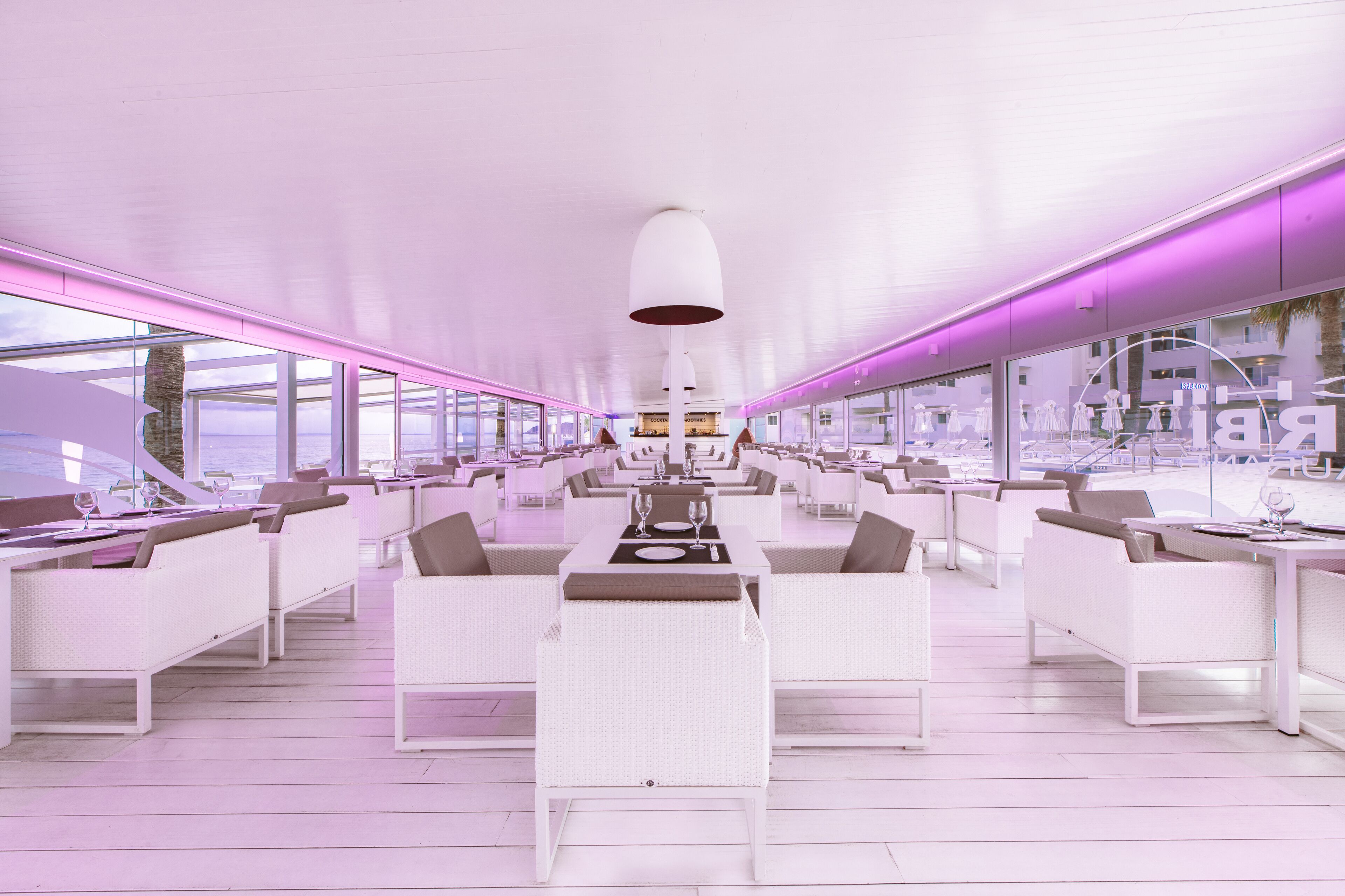 Un restaurante moderno y espacioso con mobiliario blanco y grandes ventanales que ofrecen vistas de la ciudad.