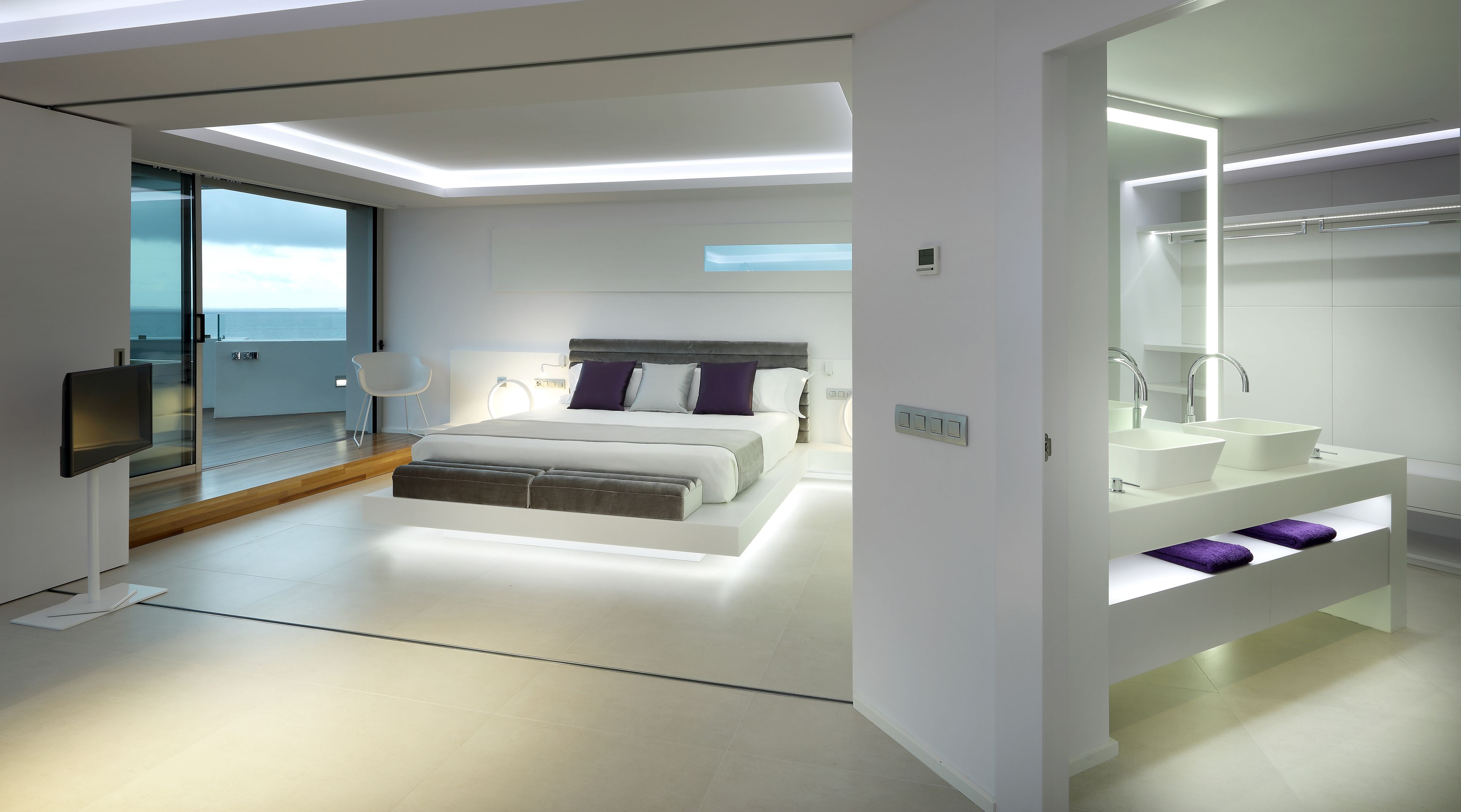 A modern bedroom with a large bed, a bedside table, a TV, and a bathroom with a sink and mirror.