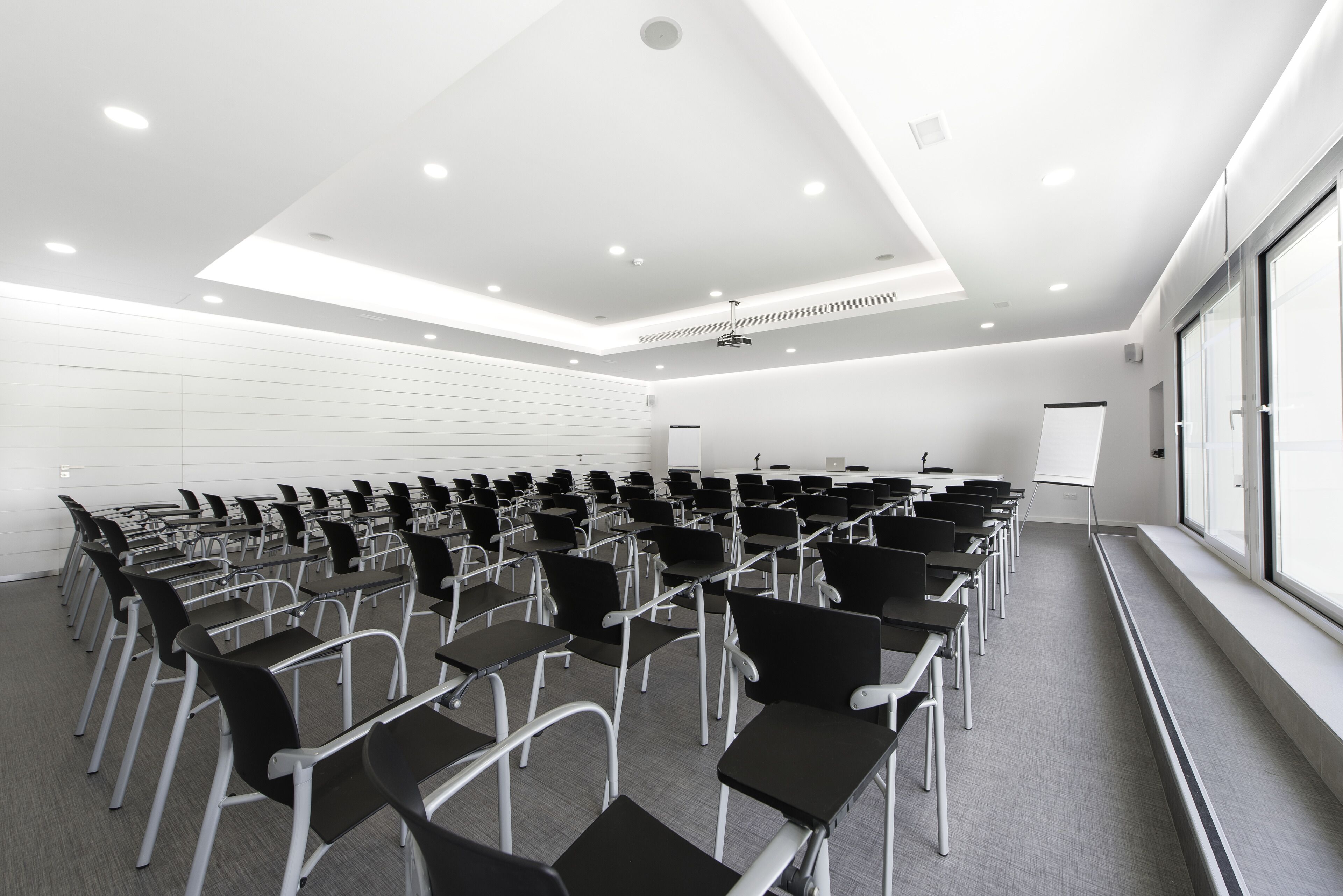 Un salón de conferencias con filas de sillas, una pizarra y un proyector.