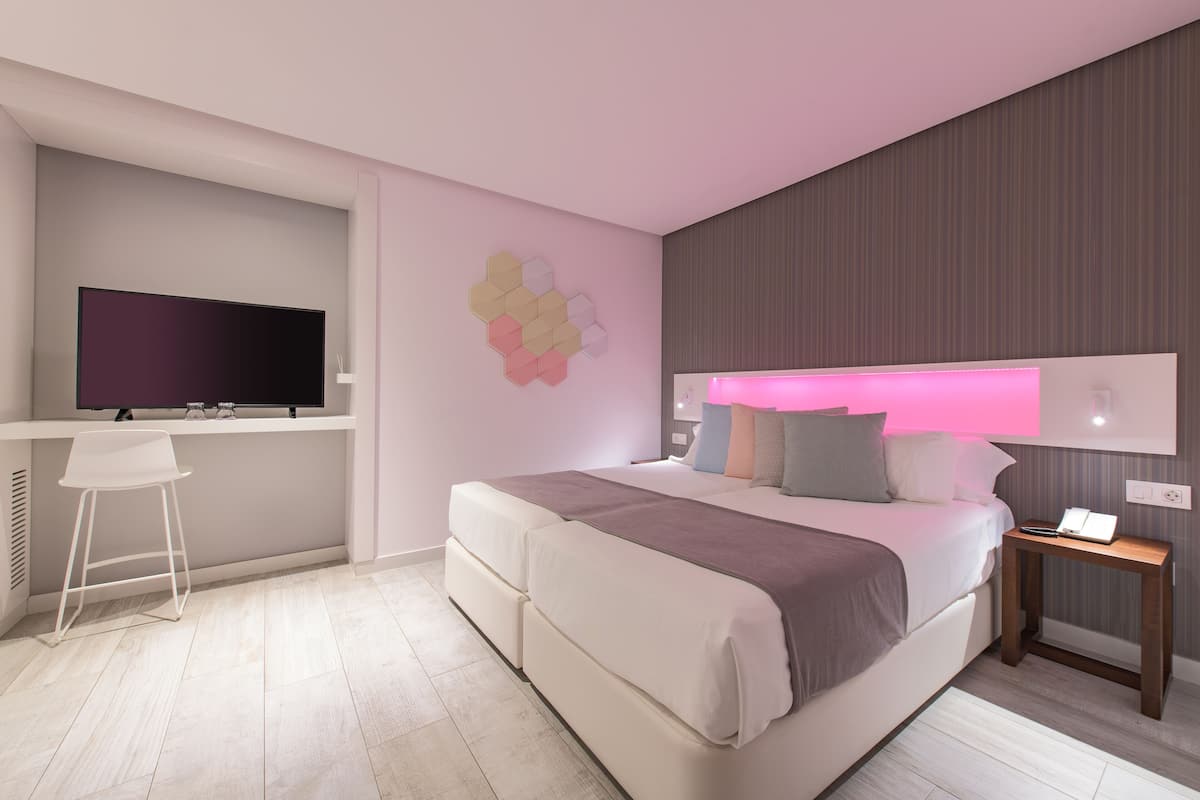A modern bedroom with a large bed, a desk with a flat-screen TV, and a wall-mounted light fixture.