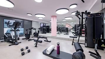 Ein Fitnessraum mit verschiedenen Trainingsgeräten, einer Bank, Kurzhanteln und einer Wasserflasche.