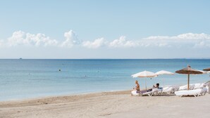 A beach with white lounge chairs and umbrellas, a clear sky, and calm sea. - Hotel Garbi Ibiza & Spa (Sant Josep de sa Talaia)