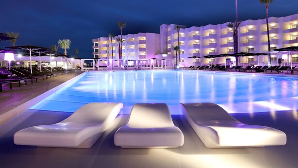 A swimming pool with lounge chairs and a building with balconies in the background. - Hotel Garbi Ibiza & Spa (Sant Josep de sa Talaia)